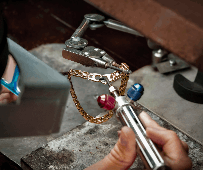 A jeweler performing precision soldering on a gold bracelet at a workbench