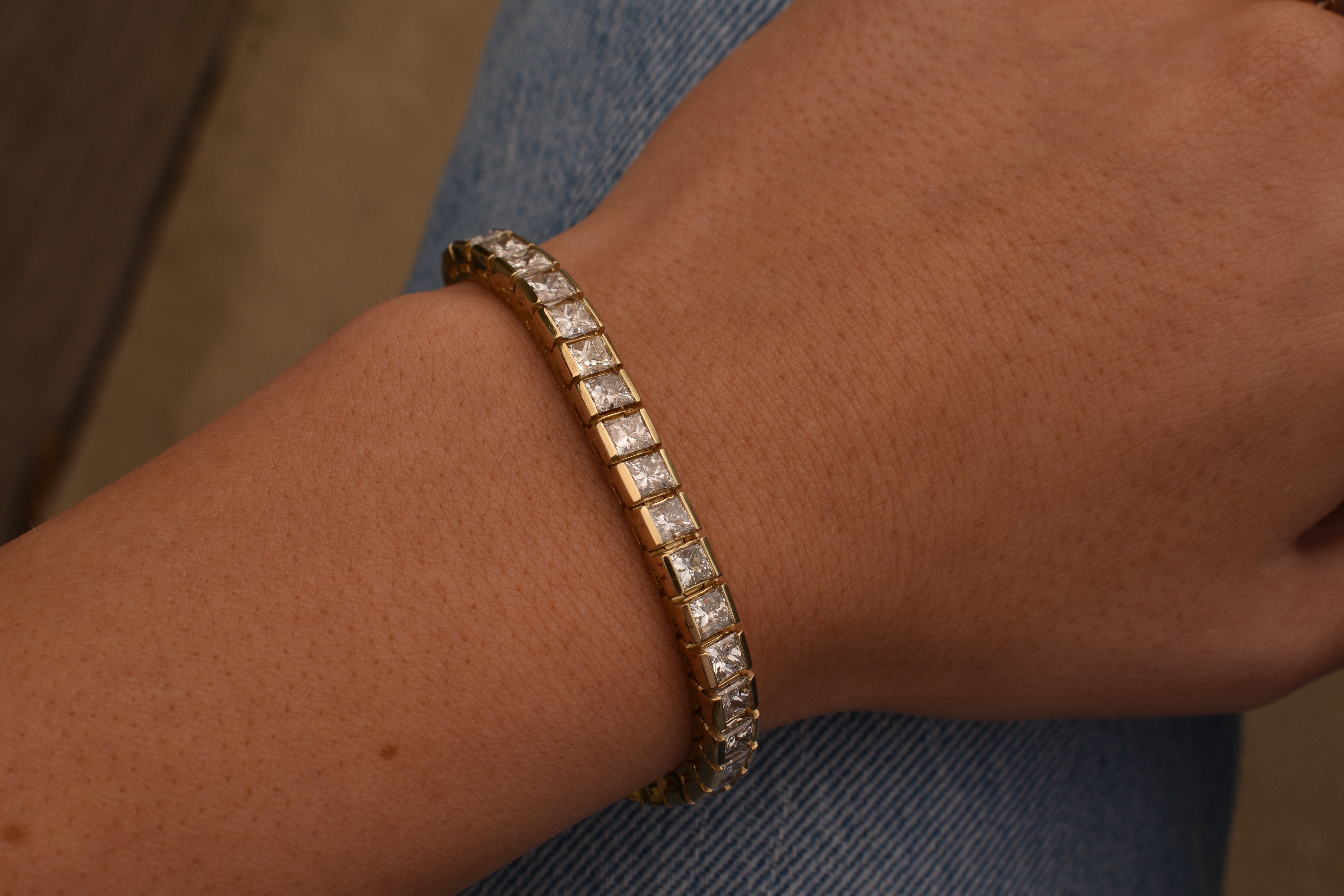 Gold tennis bracelet featuring a continuous row of princess-cut diamonds in square channel settings, worn on a wrist against a blue denim background