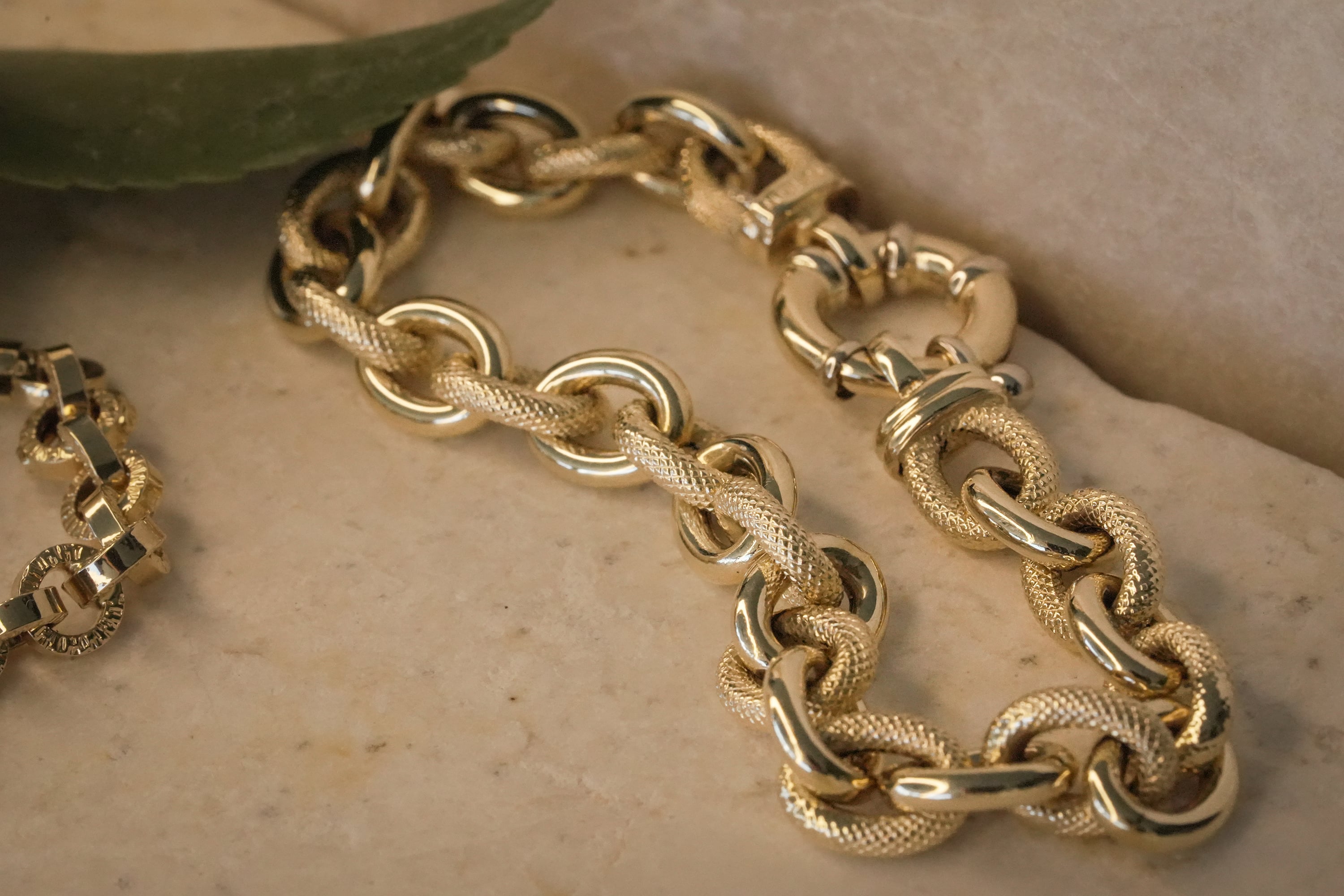Textured and polished gold link bracelet on a stone background