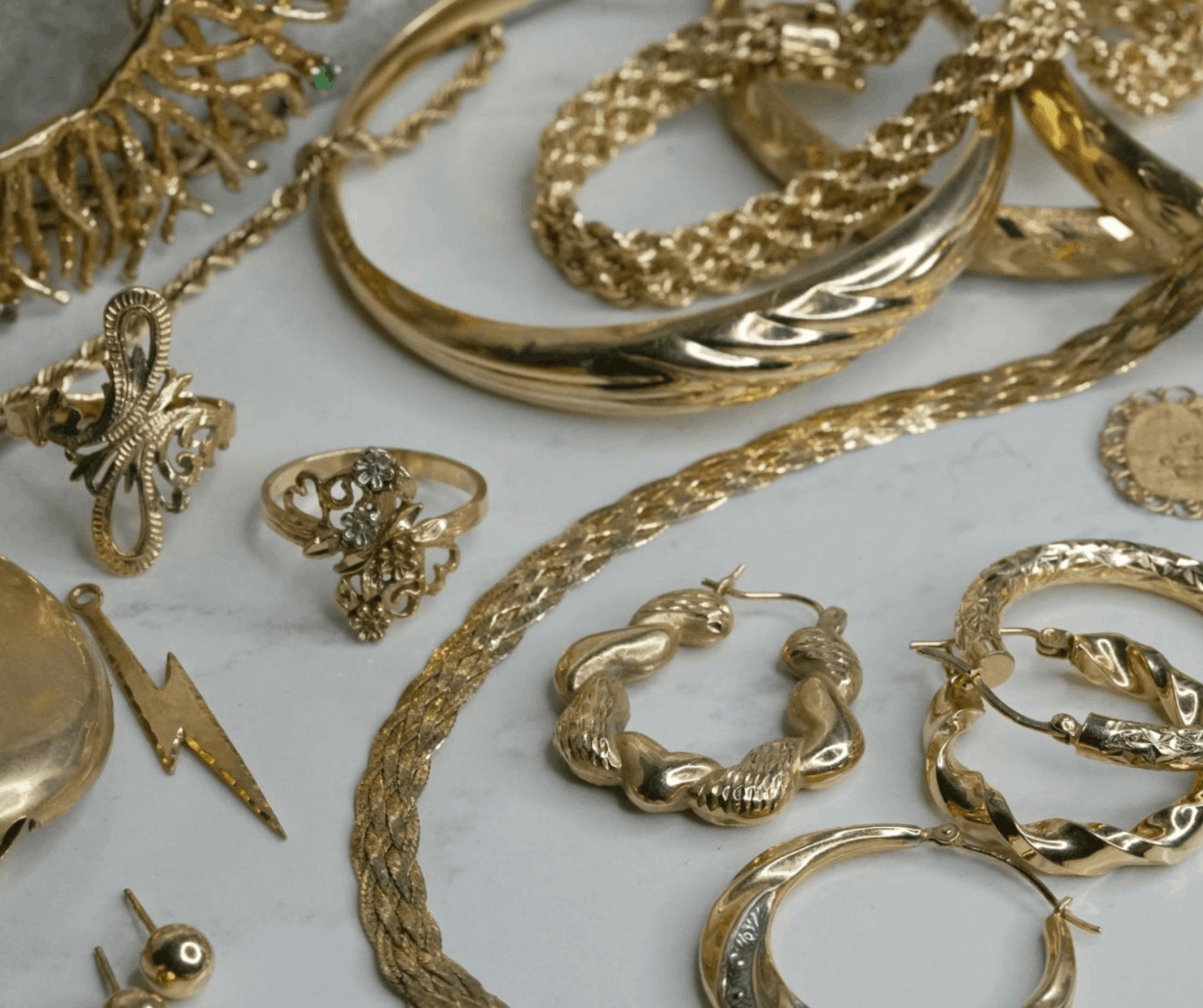 An assortment of yellow gold rings, earrings, and necklaces on a marble background
