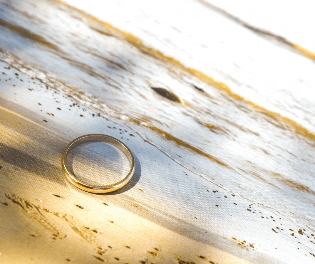 A classic yellow gold wedding band resting on a light-colored surface in the sun